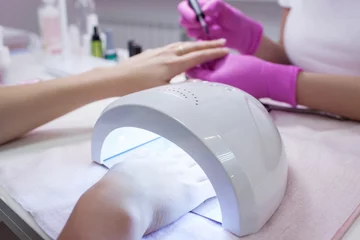  UV lamp gel polish manicure process. Salon procedure. The master coats the client's nails with a varnish. © Photodrive