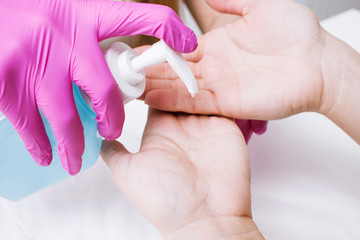 Disinfection hands before manicure in the salon closeup. Beautician is disinfecting client's with desinfectant