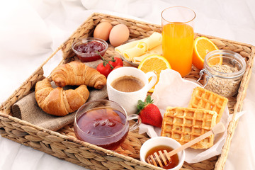 breakfast in bed with fruits and pastries on a tray -waffles, croissants, coffe and juice