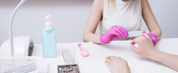 Manicurist does manicure with nail file. Professional workplace, small business, spa procedure,...