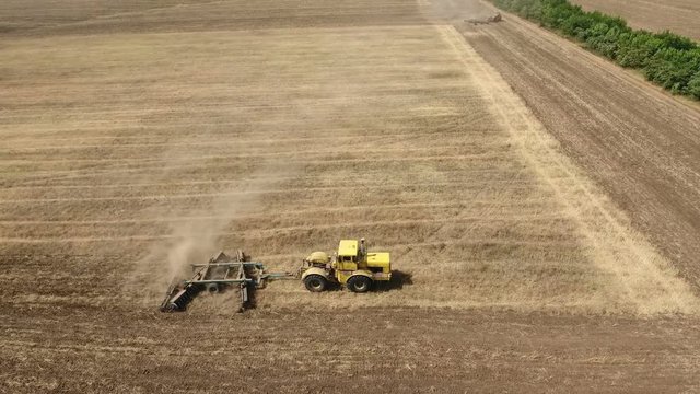 Wonderful aerial shot of a big tractor drawing a spike and a disc harrows to remove wheat straw and to do a  tillage in Eastern Europe in a sunny day in summer. The farm tractor is shot in profile 