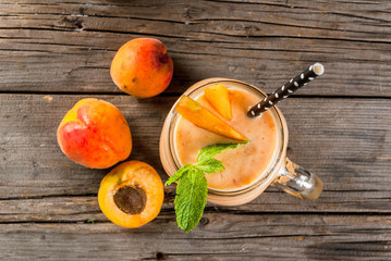 Homemade organic smoothie from yogurt and apricot. In Mason Jar, on a rustic old wooden table, with apricots and mint leaves. Copy space top view