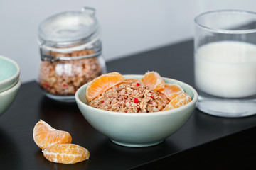 Close-up of green ceramic bowl with muesli with dried berries and fresh tangerine on the black table. Healthy breakfast concept.