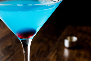 Blue Moon Cocktail with cherry on wooden surface.