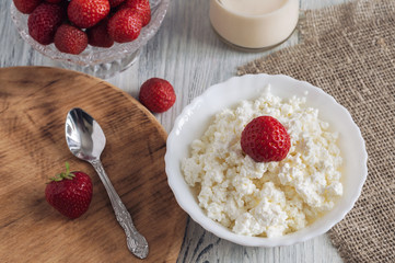 Cheese in white bowl with strawberries on wooden white table.