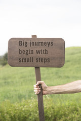 The motivational quote Big journeys begin with small steps - hand holding chalkboard with text. green nature background. 