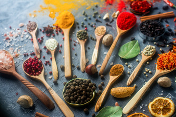 Various indian spices in wooden and silver spoons and metal bowls, seeds, herbs and nuts on dark stone table. Colorful spices, selective focus. Organic food, healthy lifestyle.