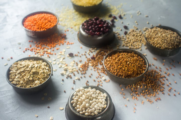 Raw organic cereal grains, seeds and beans (millet, rye,wheat, buckwheat, red and white beans, lentil, rice)  in metall bowls on light  background, selective focus. Healthy eating concept