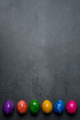 A row of multi-colored painted eggs on a dark gray stone background. Easter eggs. Happy easter frame. Copy space