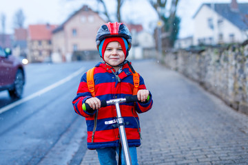 Cute little preschool kid boy riding on scooter riding to school.