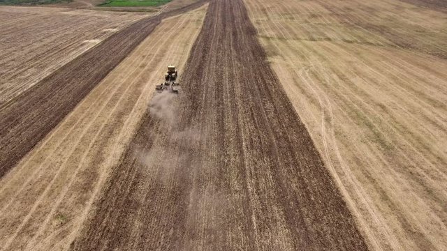 Impressive aerial shot of a big tractor drawing a spike and a disc harrows to take away wheat straw and to do a  tillage in Eastern Europe in a sunny day in summer. The tractor is shot  from behind