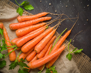 Carrots of various sizes stacked in a pile on a burlap background. Washed and ready to eat. View from above