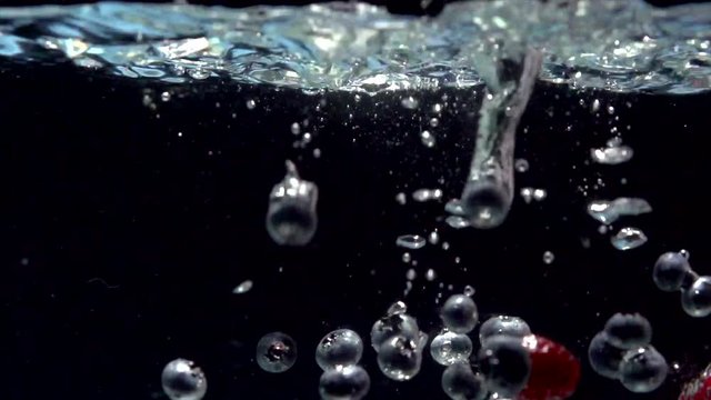 Raspberry and blueberry. Berries splashing into water on black background. 4K UHD video 3840X2160 slow motion