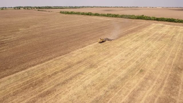 Amazing aerial shot of a yellow tractor drawing a spike and a disc harrows to remove wheat straw and to do a  tillage in Eastern Europe in a sunny day in summer. The landscape looks gorgeous