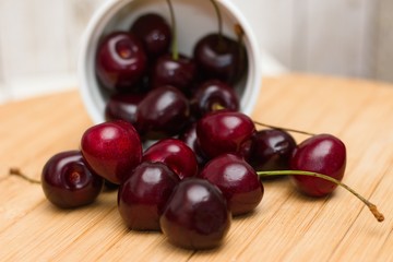 Tipped over porcelain bowl of ripe black cherries spilled on wooden table