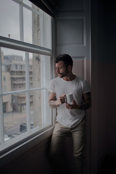 Man looking through window while holding coffee cup at home