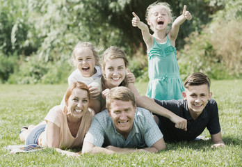 Portrait of big ordinary family lying on green lawn outdoors