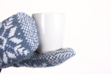 Hands in a pair of blue and white knit winter mittens holding a hot cup of coffee, tea or hot cocoa