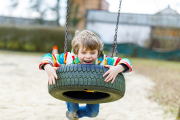 Funny kid boy having fun with chain swing on outdoor playground