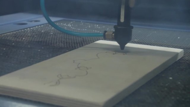 Laser torch is cutting a plywood plate. Laser cutting beam over plywood sheet