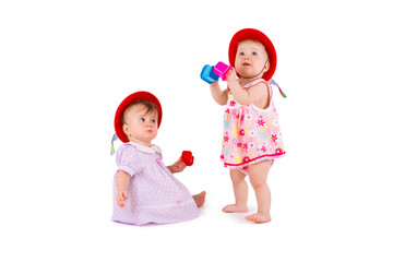 Two lovely babes in colored dresses and red hats are playing on a white background