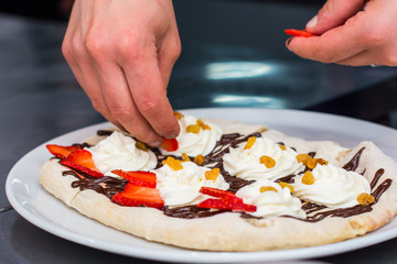 Obraz na płótnie Canvas cooking of sweet Italian pizza. Hands pizza maker put on the cream berries, raisins, strawberries
