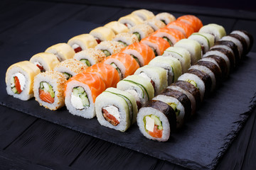 Tasty great colorful set of fresh japanese sushi maki rolls with salmon, tuna and avocado served on black slate. Food art, traditional seafood, restaurant menu photo