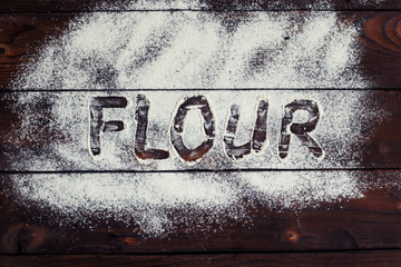 Kitchen, cooking, bakery concept. Sprinkled flour with handwritten text "Flour" on rustic wooden background, flat lay.