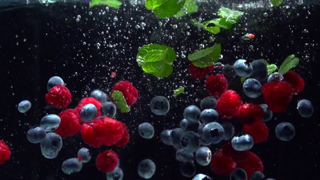 Raspberry and blueberry. Berries splashing into water on black background. 4K UHD video 3840X2160 slow motion