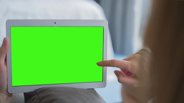 Young Woman in white top sitting on sofa uses Tablet PC with pre-keyed green screen. Few types of gestures - scrolling up and down, tapping, zoom in and out. Perfect for screen compositing