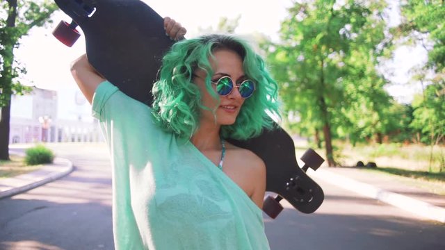 Young woman with green hair walks with long board in slow motion