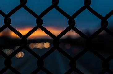 Fototapeta premium Chain link fence with depth of field, out of focus sunset. Sunset with amazing sunset background. Industrial sunset.
