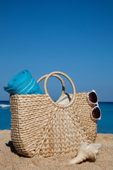 Summer straw bag with blue towel and sunglasses on a tropical sandy beach
