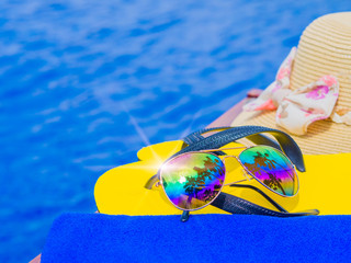 Sunglasses with summer hat, flip flops by the swimming pool. Vacation and relaxation, summer travel concept.