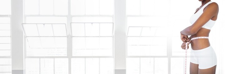 Slim healthy woman holding measuring tape  by windows