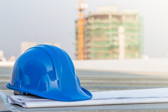 The blue safety helmet and the blueprint at construction site with crane background