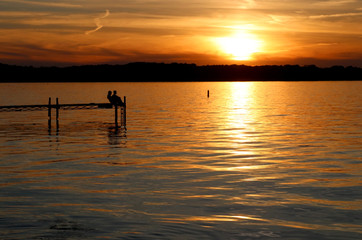 Summer sunset over the lake. Landscape with golden sunset and silhouettes of people enjoying the beautiful evening on a lake Mendota pier in the city of Madison, Wisconsin, USA.