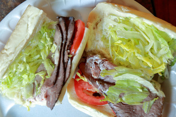 Roast beef submarine sandwich cut in two with bun open to show meat, tomatoes, and lettuce with mayo