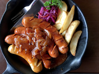 Fried sausages with garlic, herbs and french fries in a pan. On the table black Board. still life food.