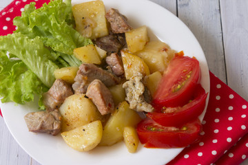 Potatoes with meat and vegetables on a white plate. Tasty and hearty dish.