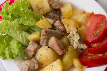 Potatoes with meat and vegetables on a white plate. Tasty and hearty dish.