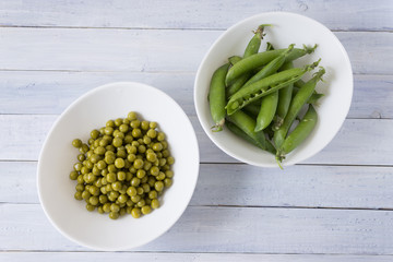 Fresh and canned peas in white bowls on a wooden table
