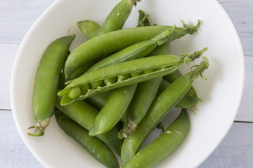 Fresh green peas in a white bowl on a wooden table