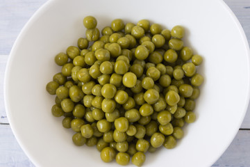 Canned green peas in a white bowl on a wooden table