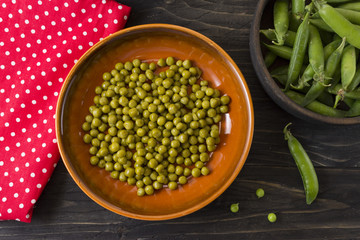 Canned green peas in a clay bowl and fresh peas in a wooden bowl on a wooden table. Healthy food.