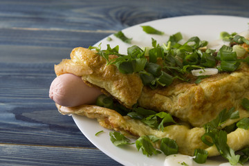 Omelette with sausages, cheese and greens on a white plate. Delicious and nutritious breakfast.