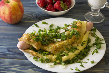 Omelette with sausages, cheese and greens on a white plate. Delicious and nutritious breakfast.