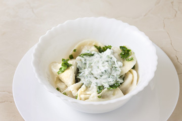 Homemade pelmeni or meat dumpling with sour cream and parsley. Traditional Russian cuisine.