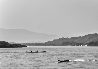 Fototapeta premium Black and white monochrome image of two boats sailing on Mekong river with forest and mountain on background