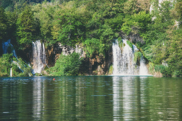 Fototapeta na wymiar Waterfall at beautiful green summer forest lake